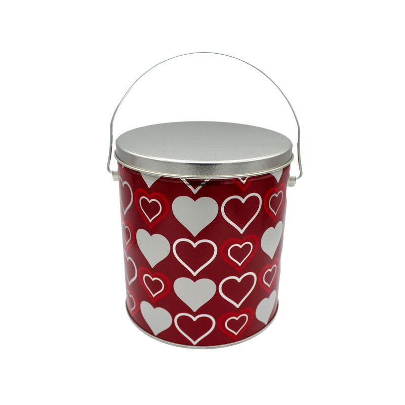 Red popcorn tin with a grey lid. The tin is covered in a three heart pattern. 1. Double outline heart (red inside white) 2. Solid white heart. 3. single white outline
