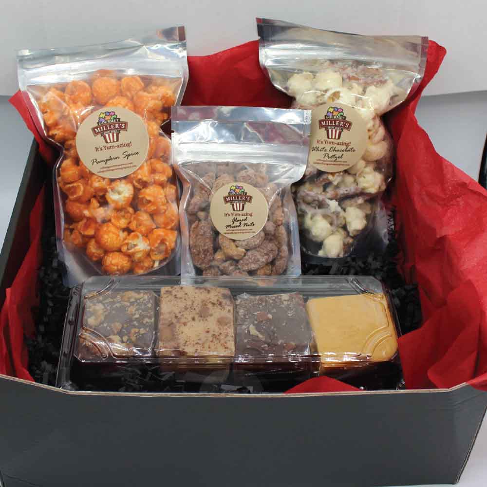 gift box display featuring: Pumpkin spice popcorn, white chocolate popcorn, glazed nuts, and four squares of fudge. The box is lined with red tissue paper.